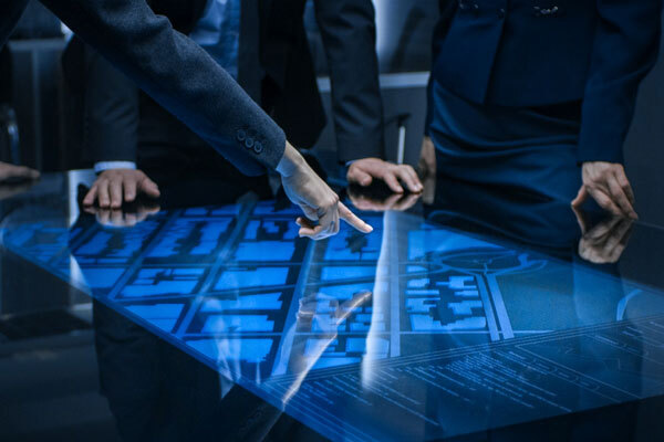 An image of men around a desk pointing at blueprints